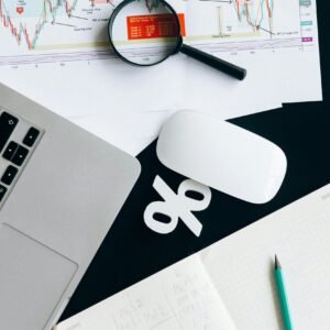 Top view of financial documents with magnifying glass, laptop, and notebook.